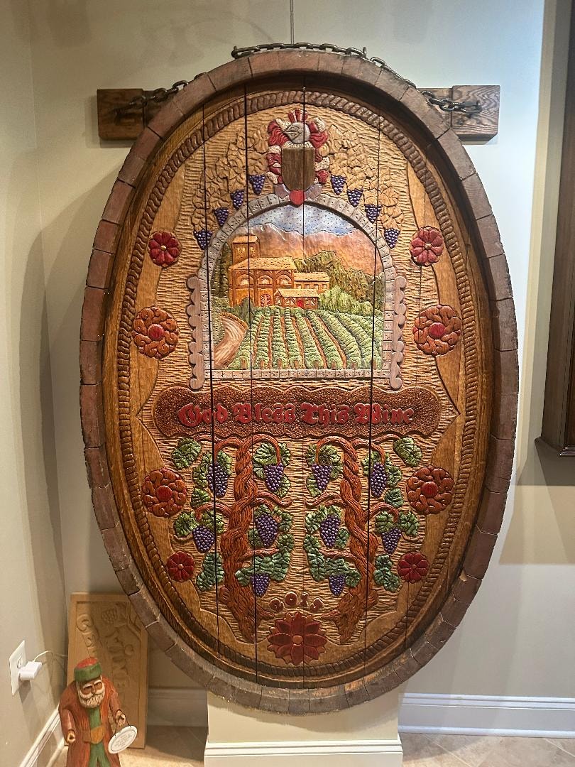 The completed God Bless This Wine cask end hanging on chains in the tasting area, fully carved and painted