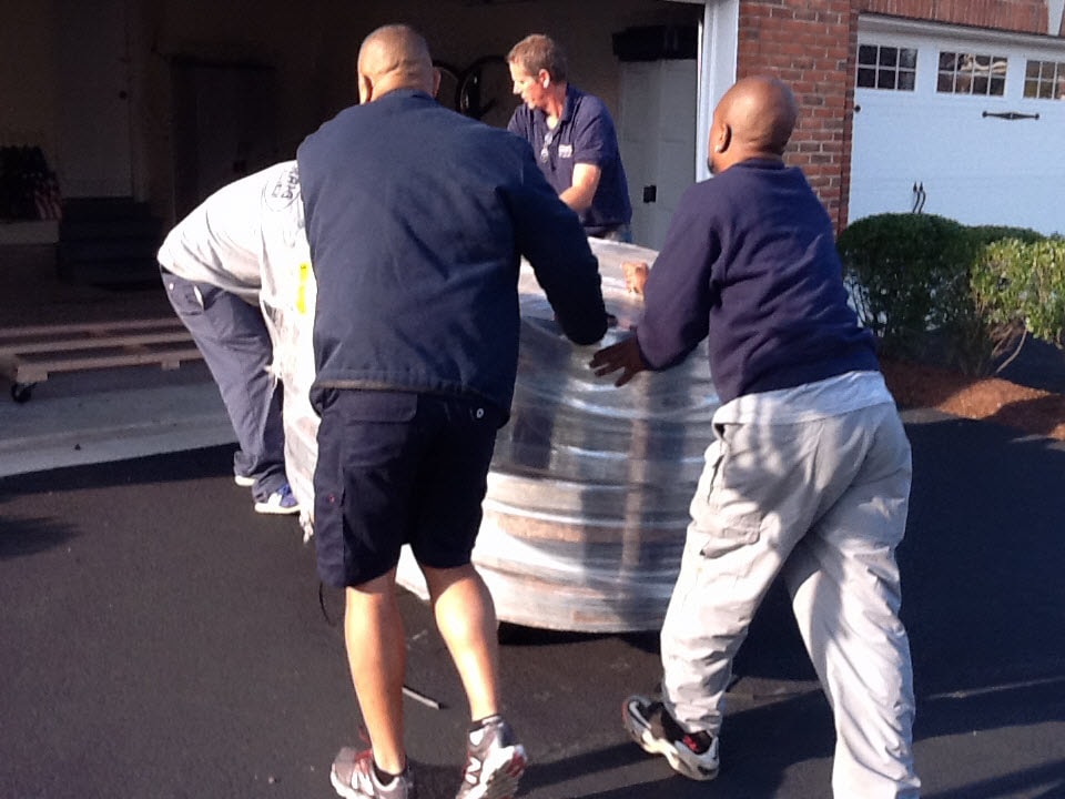Three men rolling a large wrapped wine cask across a driveway into a garage in Haymarket, Virginia