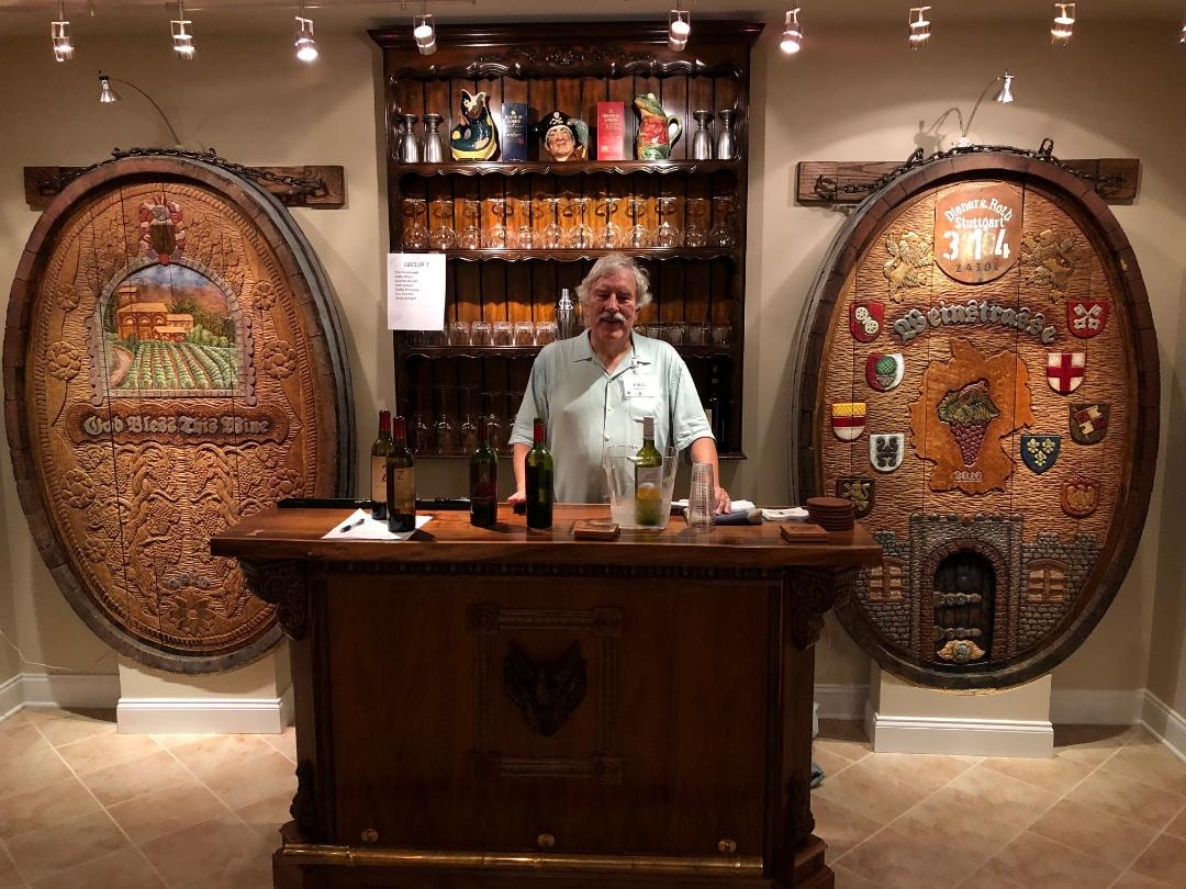 The artist standing at the tasting bar flanked by the God Bless This Wine and Weinstrasse cask ends mounted on the walls